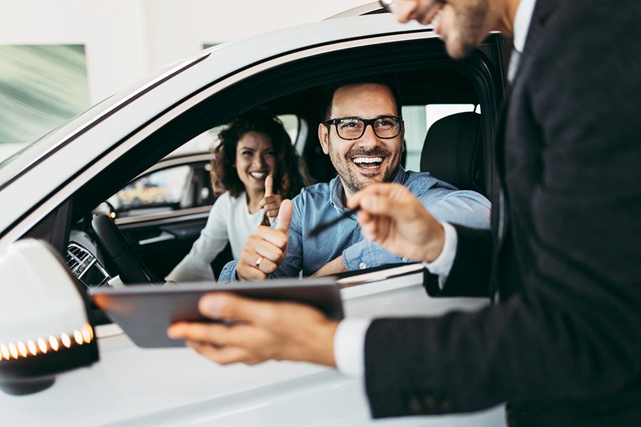 A man sitting in car smiling while talking with another man.